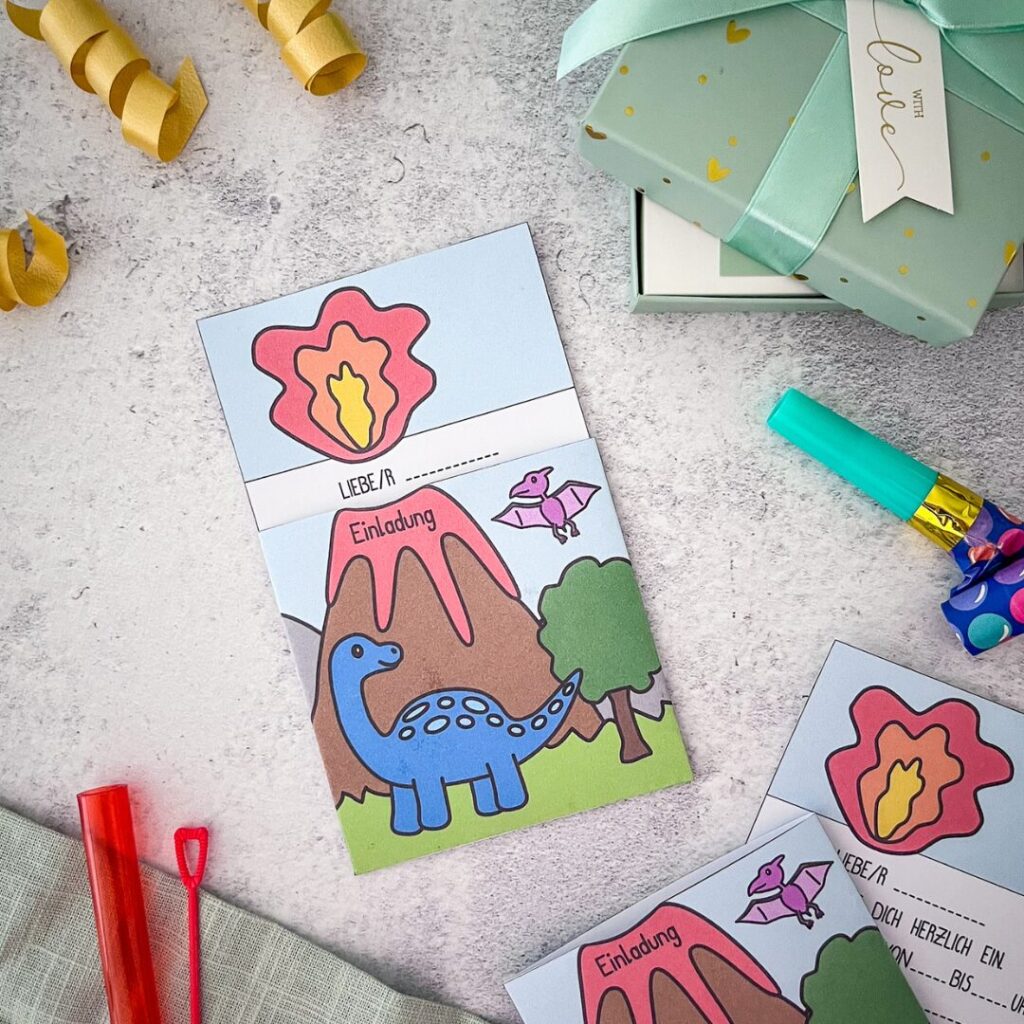 Druckvorlage für eine Einladung zum Dino Geburtstag. Gezeigt wird ein blauer Dino vor einem spuckenden Vulkan. Die Lava lässt sich herausziehn und der vorausgefüllte Einladungstext erscheint.